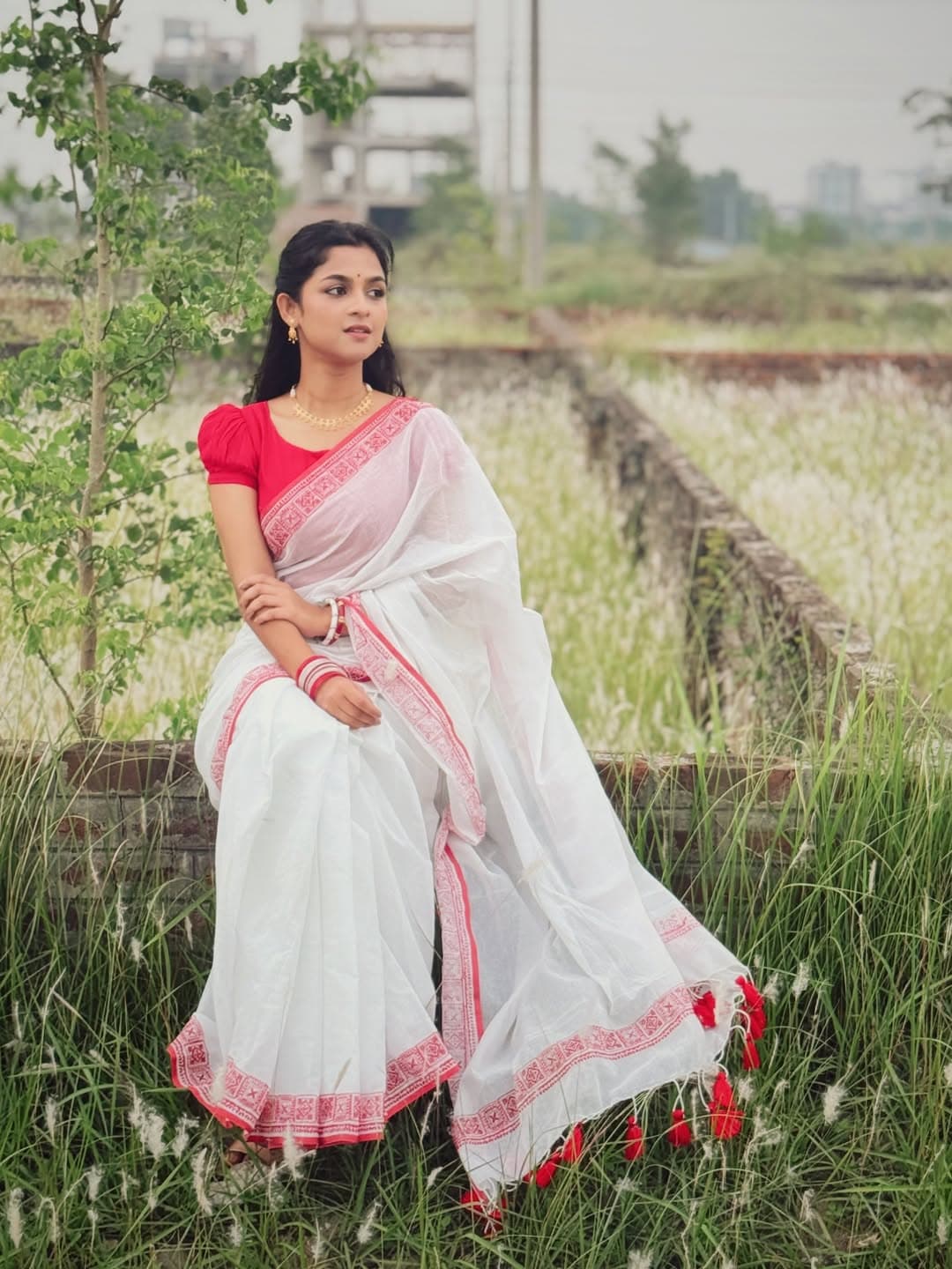 লাল পাড়ের সাদা শাড়ির সাথে লাল ঘটিহাতা ব্লাউজ, লালসাদা চুড়ি, লাল টিপ আর হালকা সোনার গয়নায় নজর কেড়েছেন সাদিয়া আয়মান।